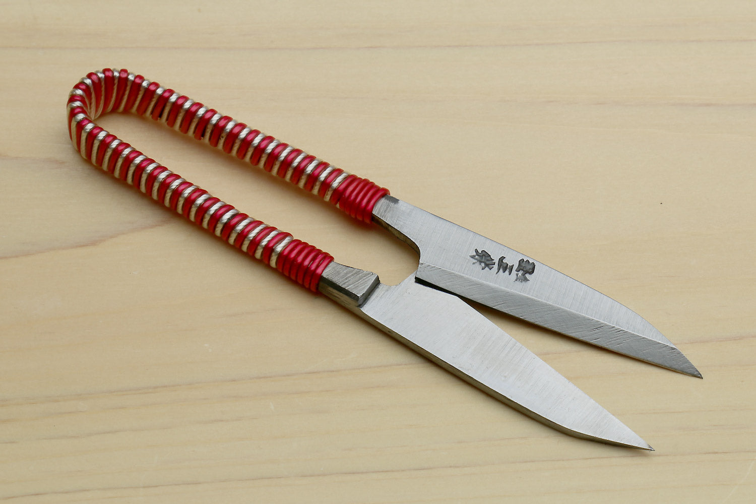 Japanese sewing snip scissors laid flat, red string-wrapped handle and pointed blades