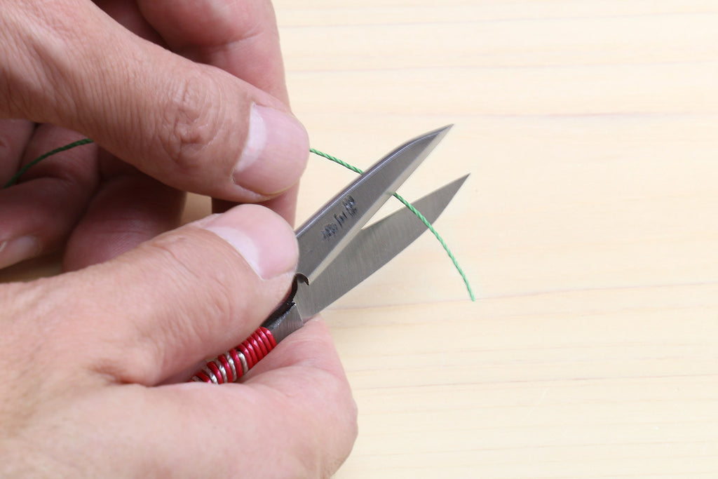 Japanese sewing snip scissors, red string-wrapped handle, blades open in hand