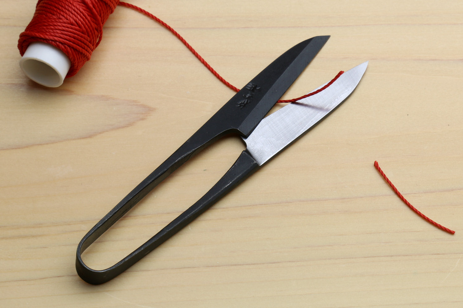 Sewing snip scissors with black handle and silver blades beside red thread
