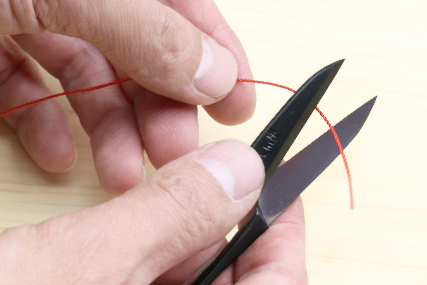 Sewing snip scissors held in hands with red thread near the blades