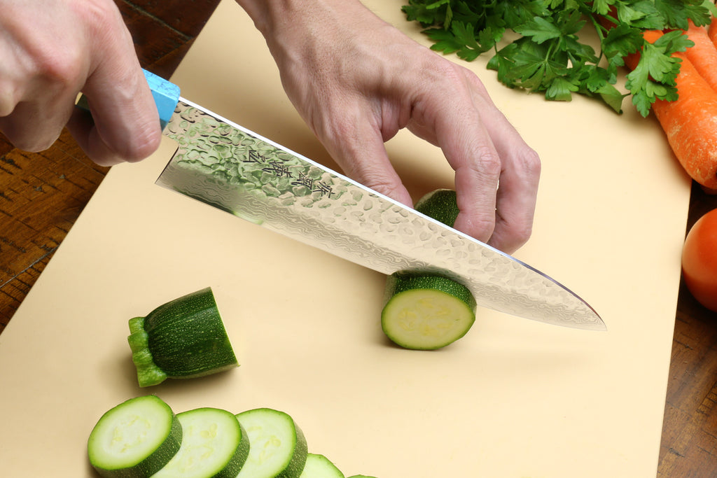 Chef's gyuto knife in hand with hammered Damascus blade over a cutting board