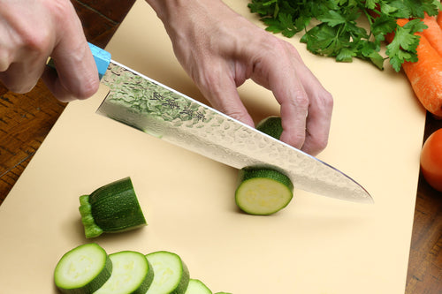 Chef's gyuto knife in hand with hammered Damascus blade over a cutting board