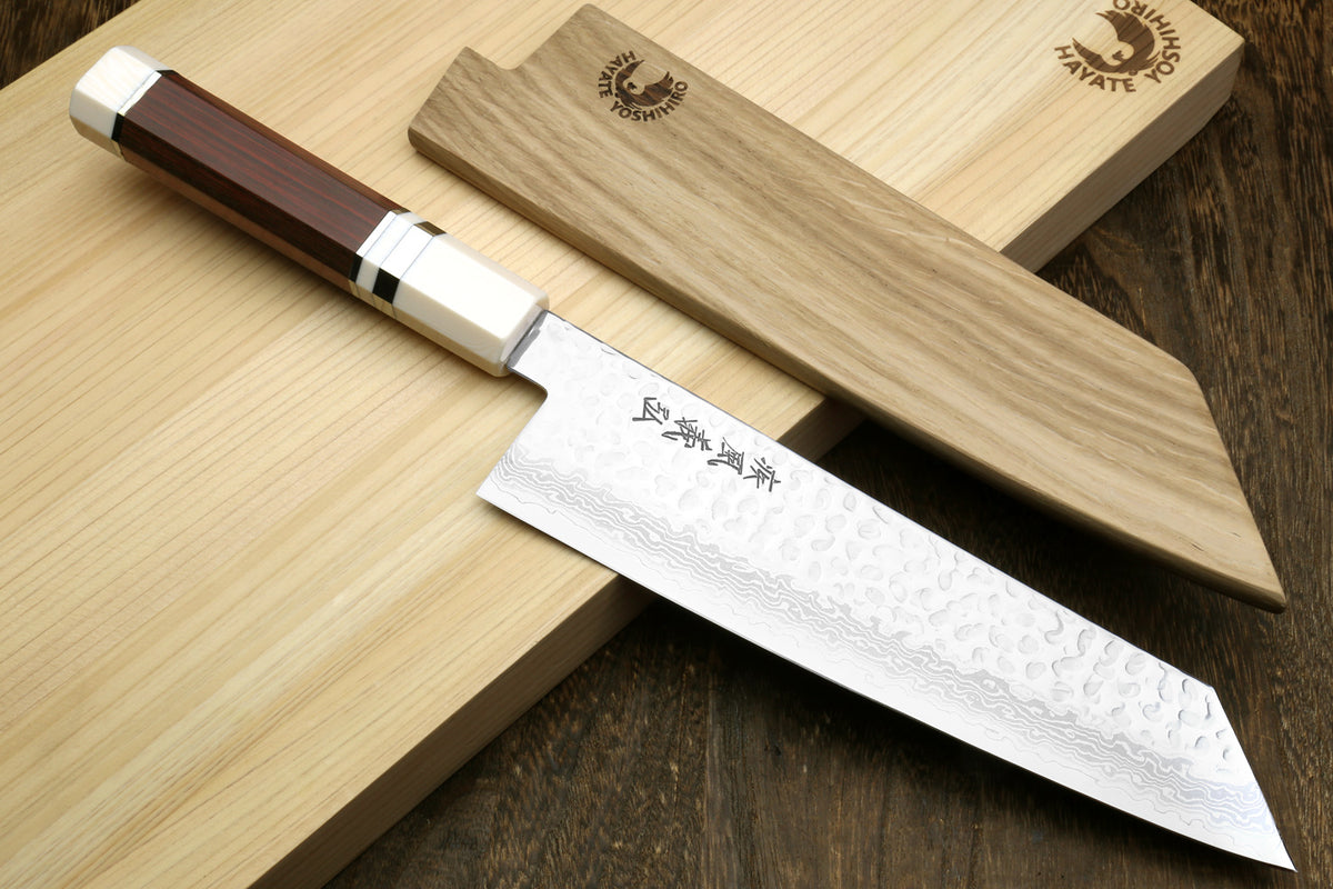 Kiritsuke chef knife with Damascus blade and octagonal rosewood handle beside wooden block