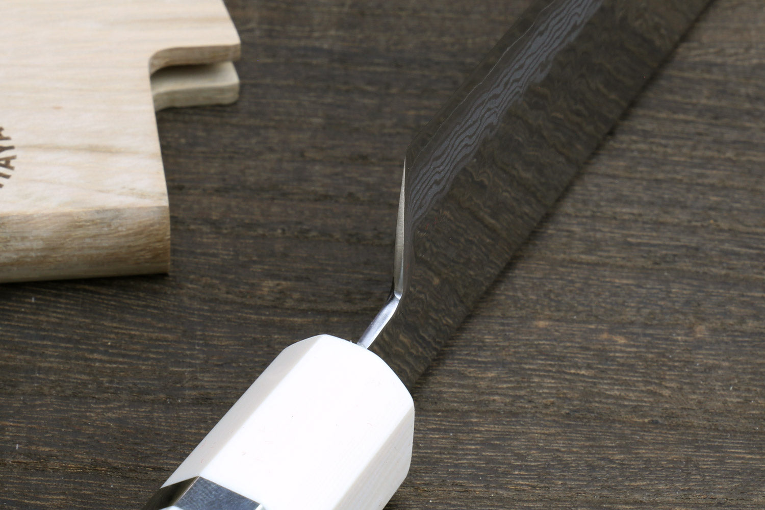 White howlite santoku handle with ivory-toned bolster and damascus blade edge close-up