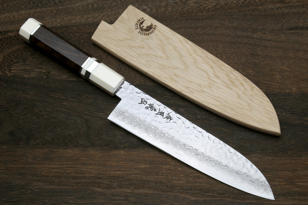 Damascus Santoku knife laid with wooden saya, light octagonal handle and dark blade.