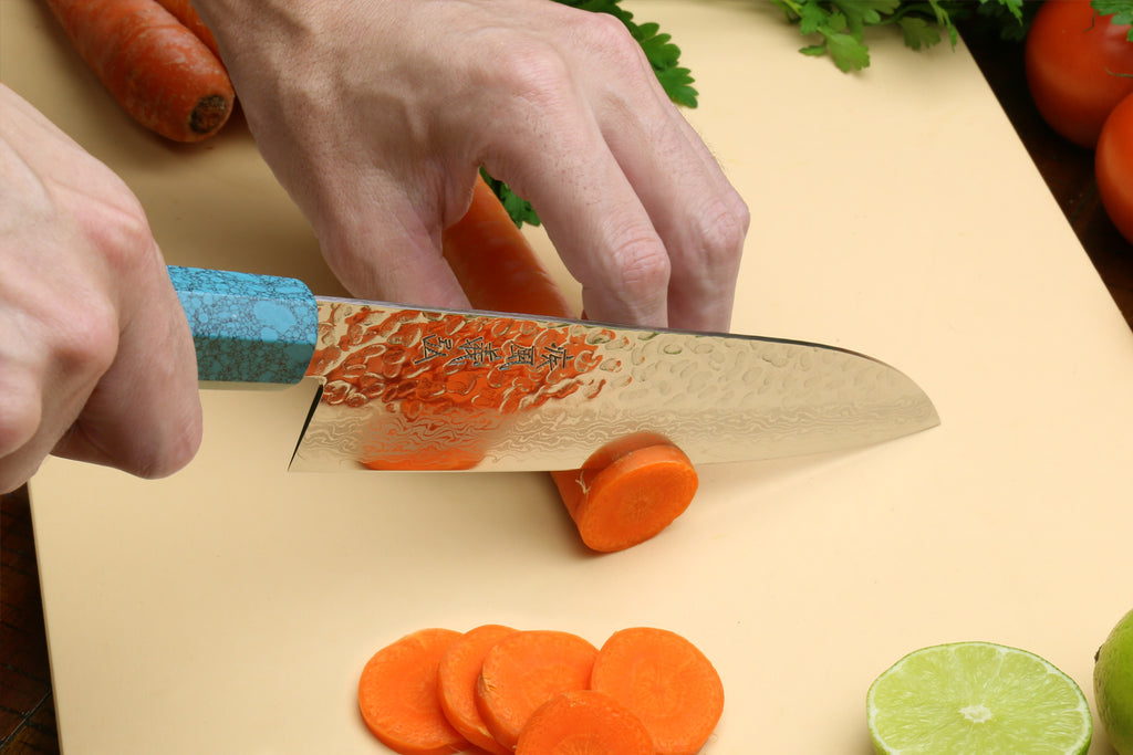Hand slicing with Santoku knife; turquoise blue octagonal handle and Damascus blade