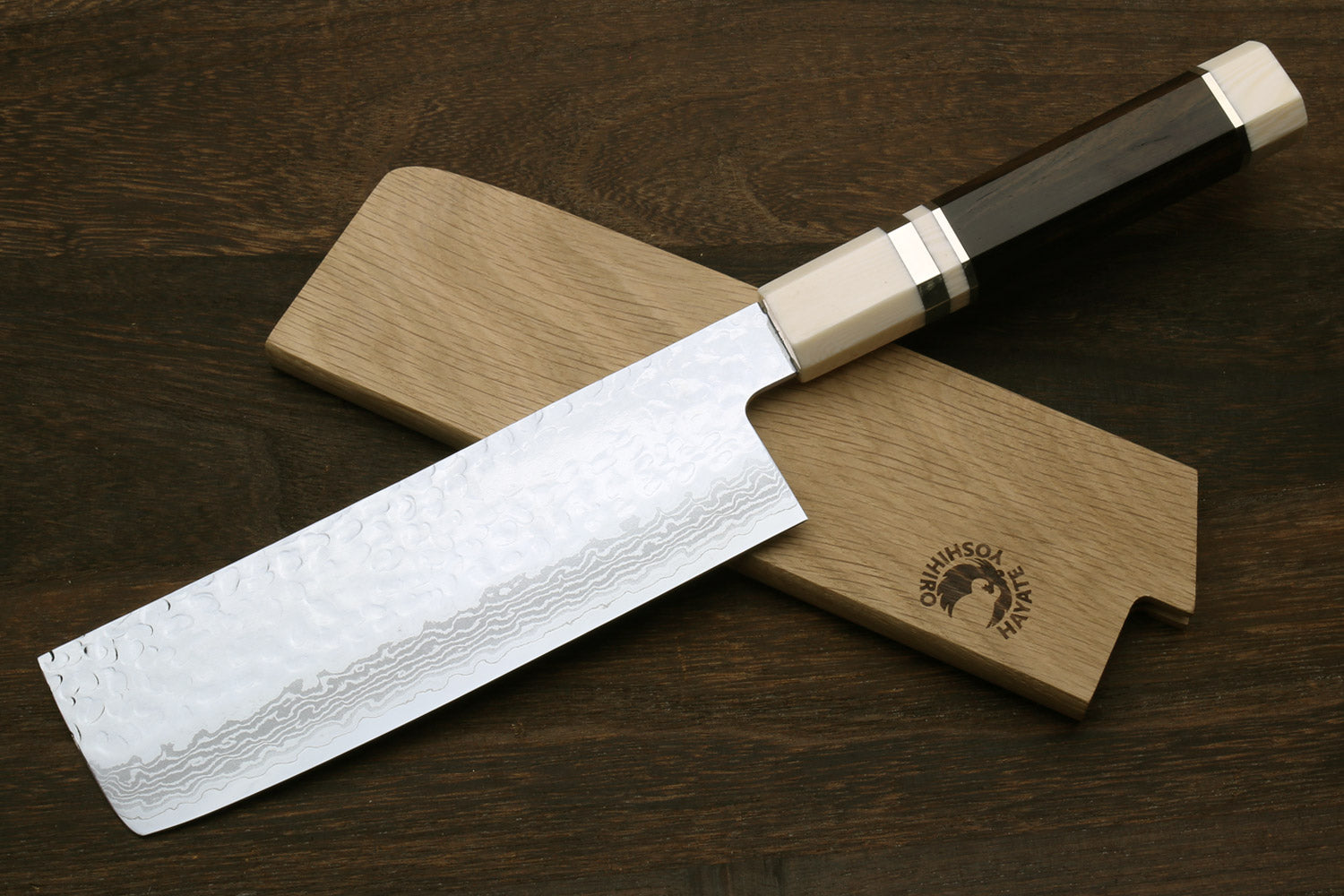 Nakiri vegetable knife with white damascus blade, dark handle, and light wooden saya sheath