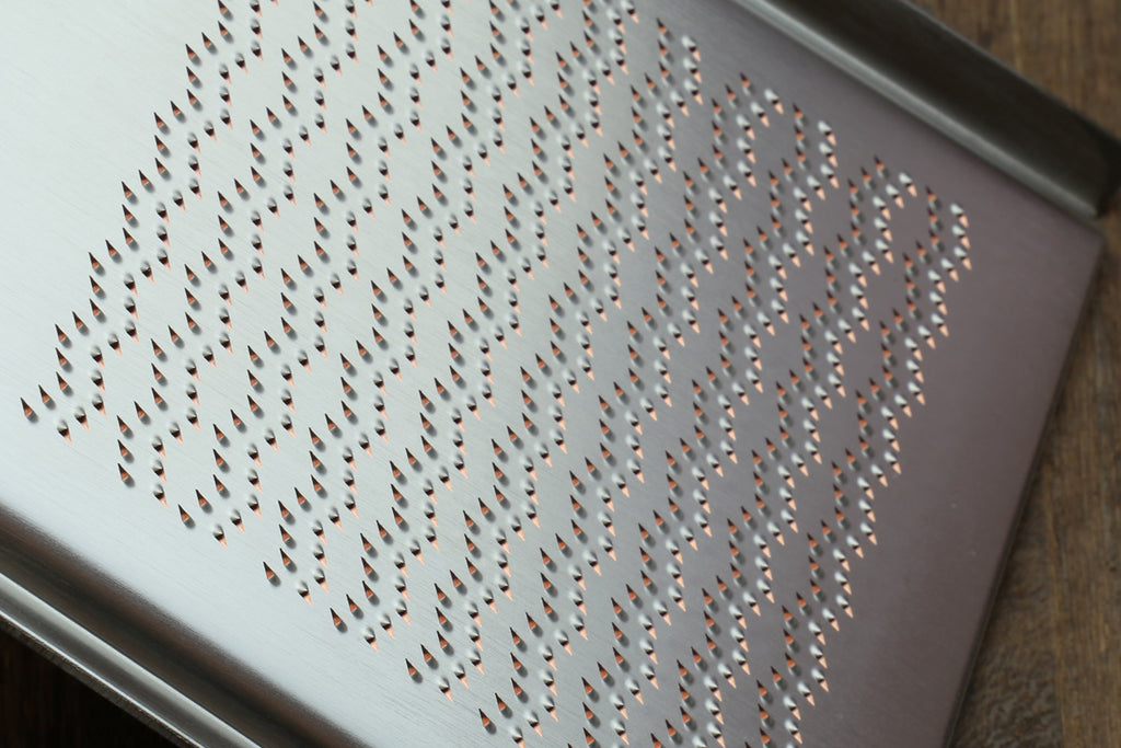 Close-up of radish grater perforations on stainless plate