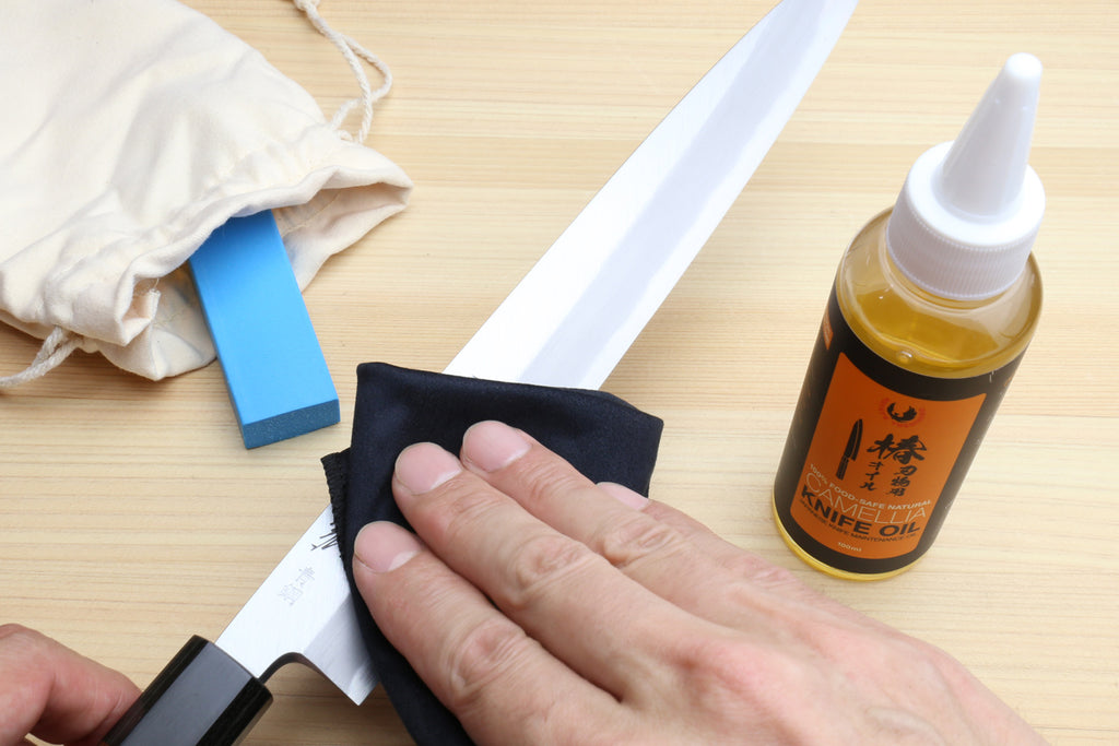 Hands wiping a knife blade with polishing cloth and oil bottle