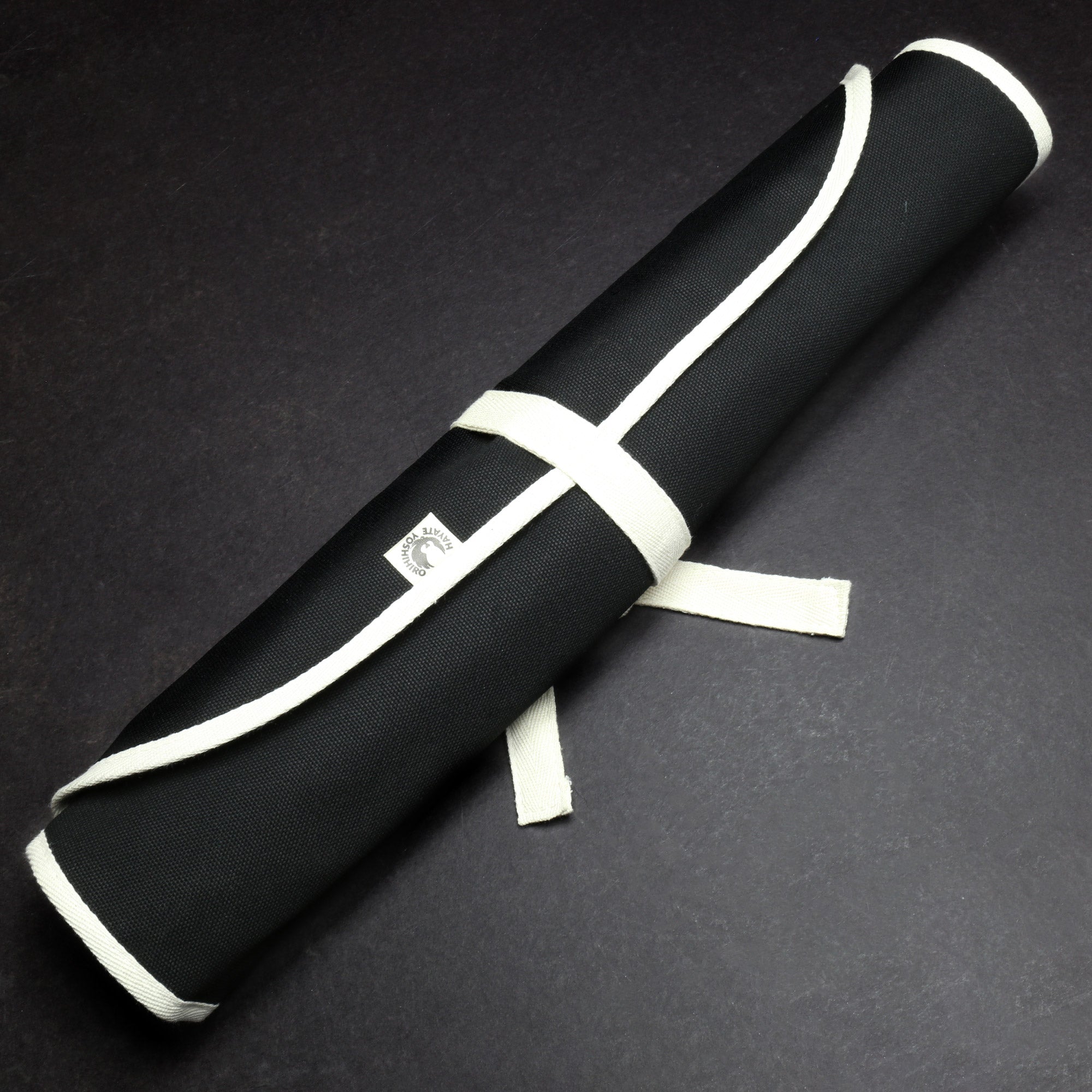 Rolled black cotton knife pouch with white wrap ties and small logo patch