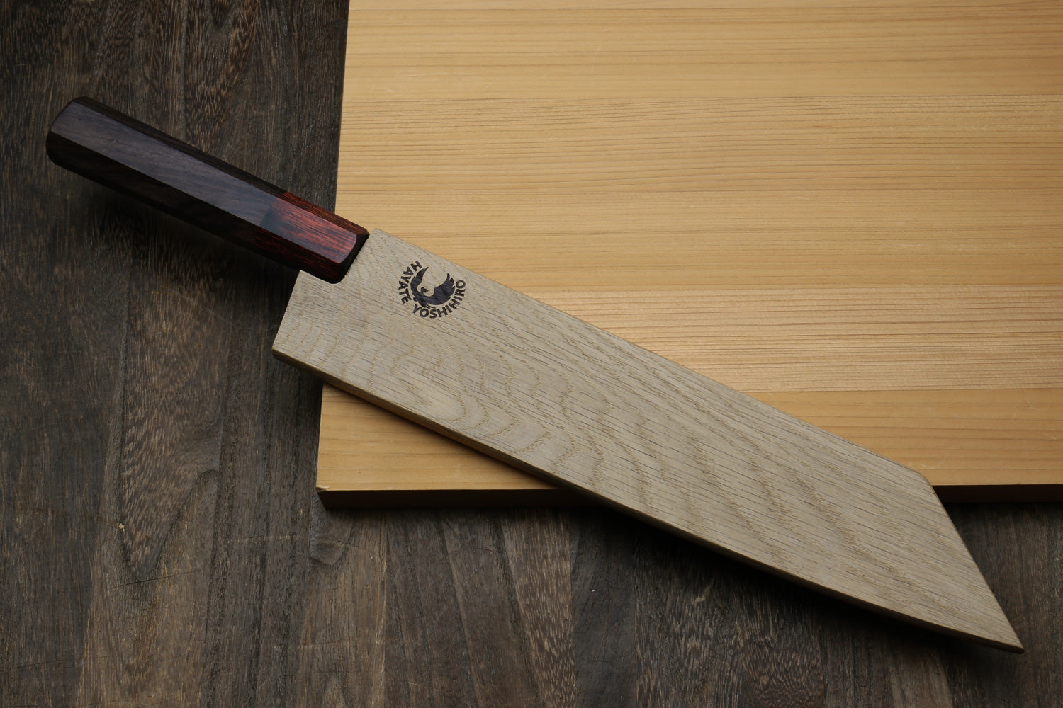 Light oak saya cover with logo, placed over a blade with dark handle