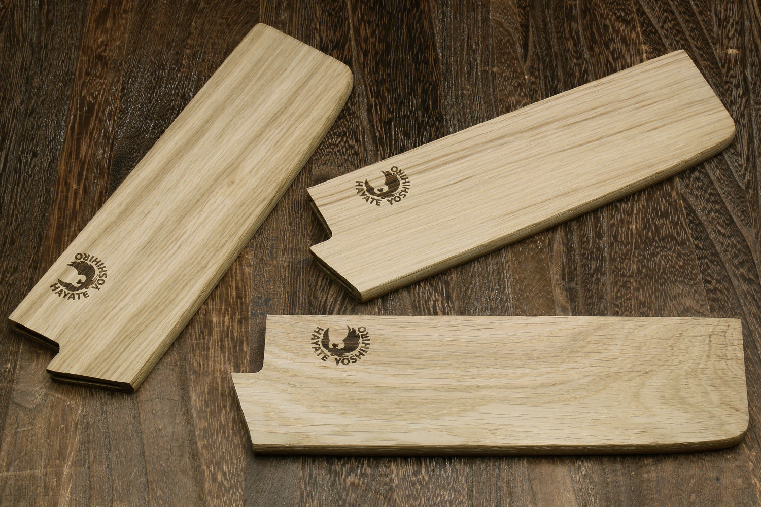 Multiple oak wood saya blade covers with embossed logos, shown laid out