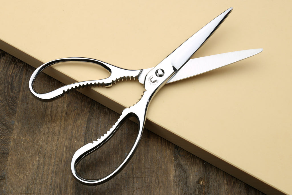 Large stainless kitchen shears with white handles and scalloped lower blade