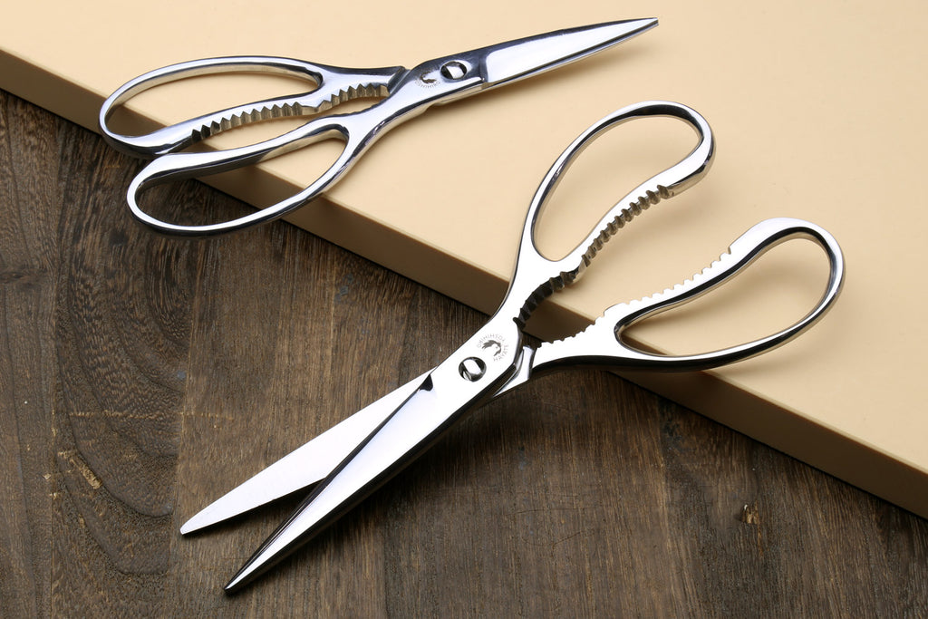 Stainless kitchen scissors with white handles, pointed blades and serrated grip