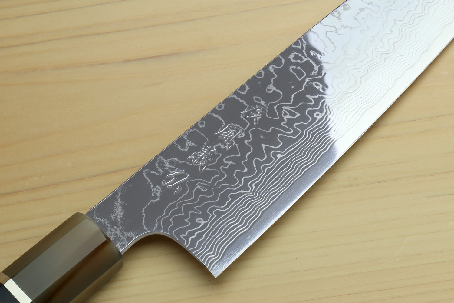 Damascus chef knife blade close-up with dark wavy pattern and sharp edge