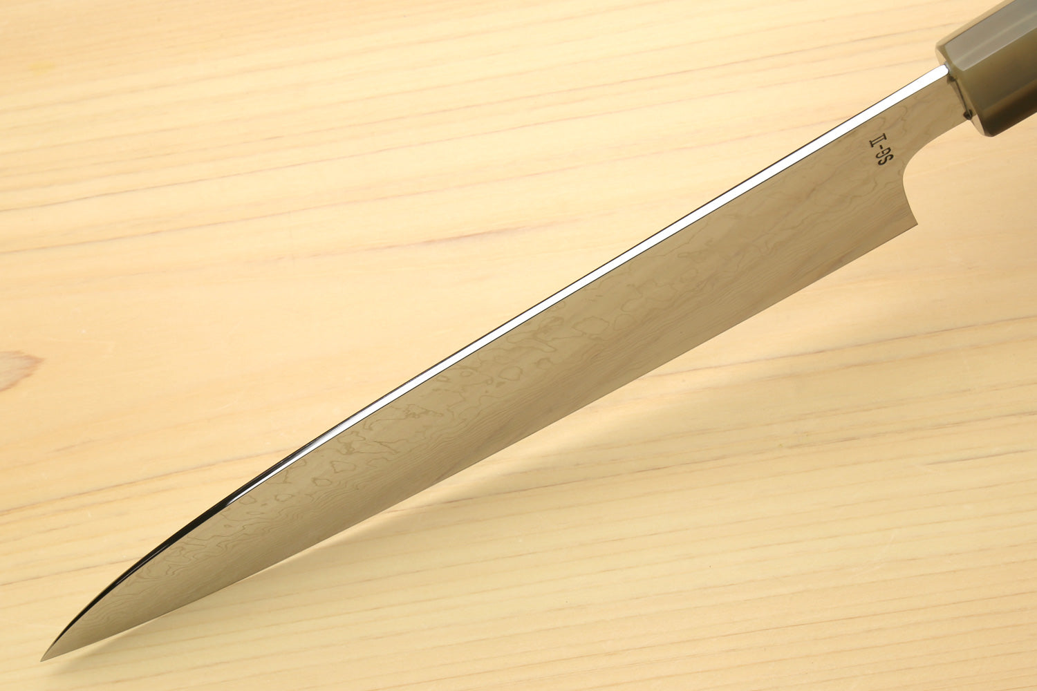 Chef knife blade side view with pointed tip and patterned steel near spine