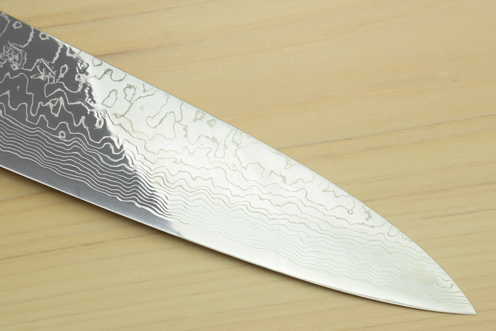 Chef knife blade close-up showing dark Damascus pattern flowing to the tip