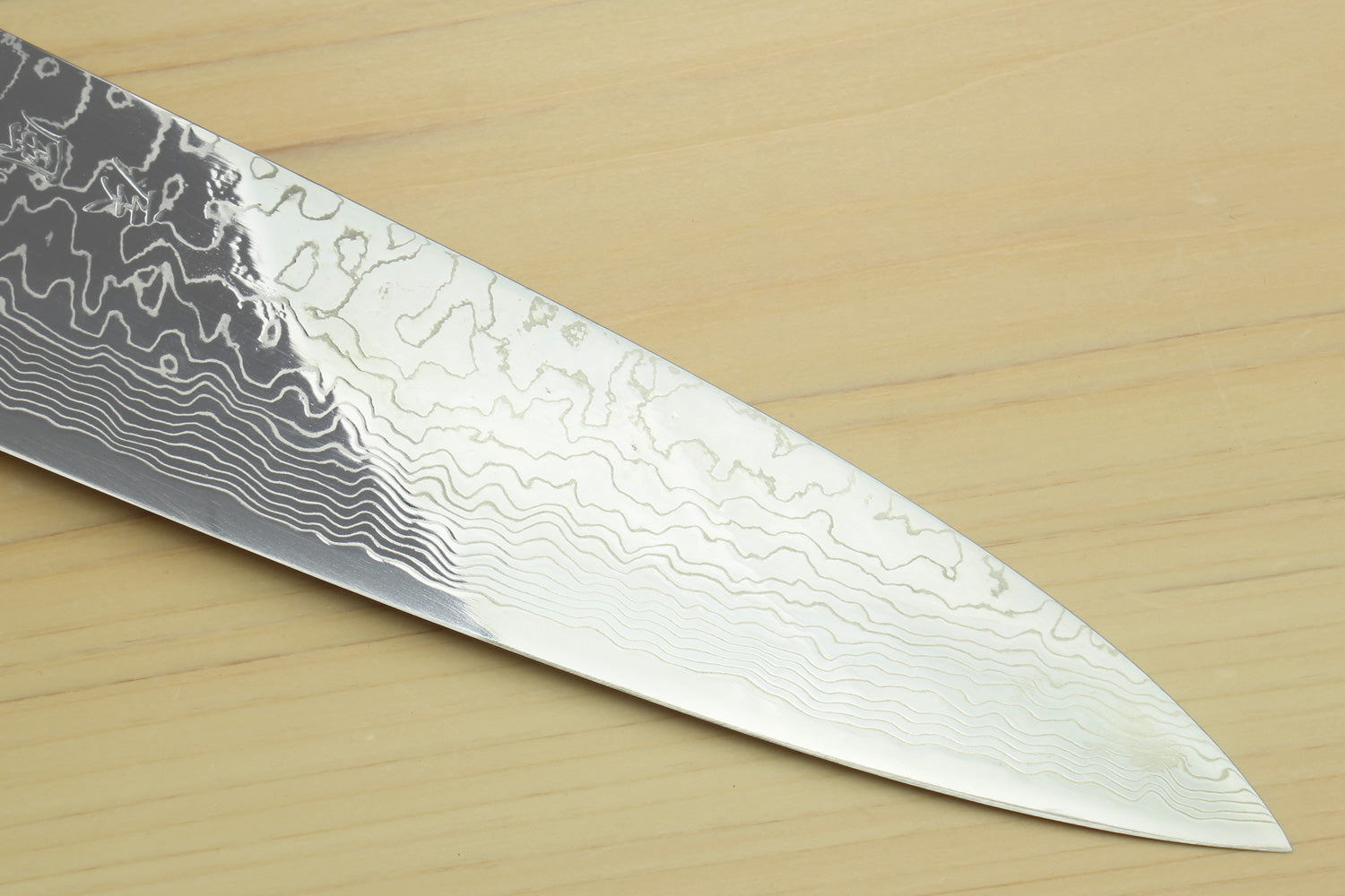 Chef knife blade close-up showing dark Damascus pattern flowing to the tip