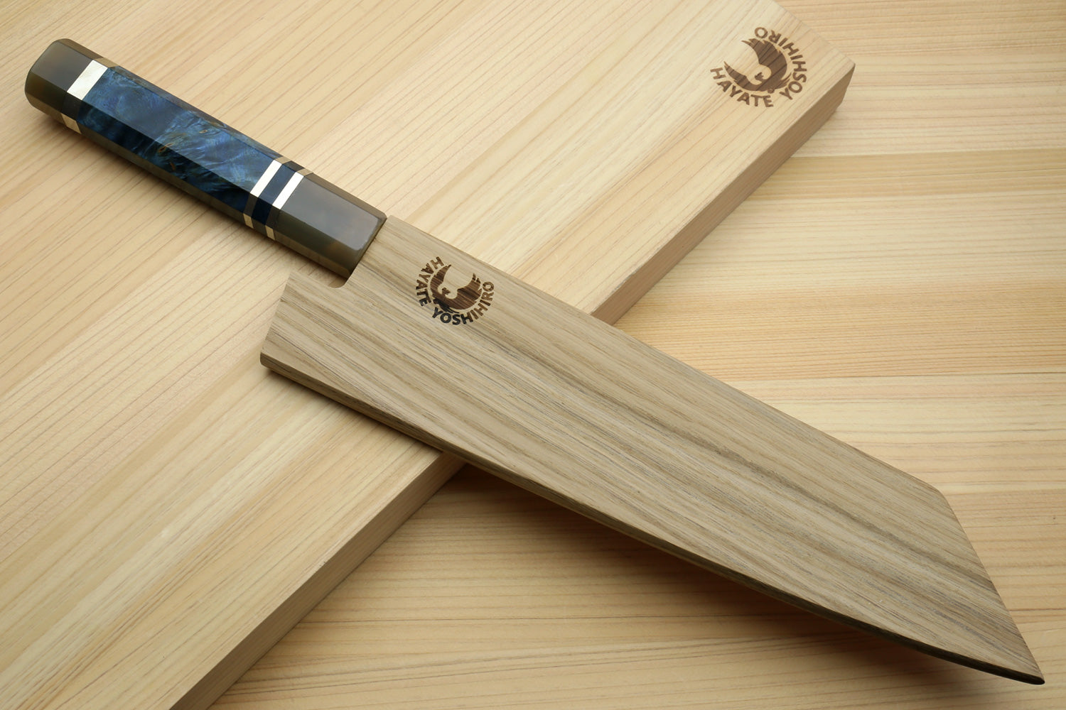 Kiritsuke chef knife with ocean blue handle and Damascus blade on light wood tray