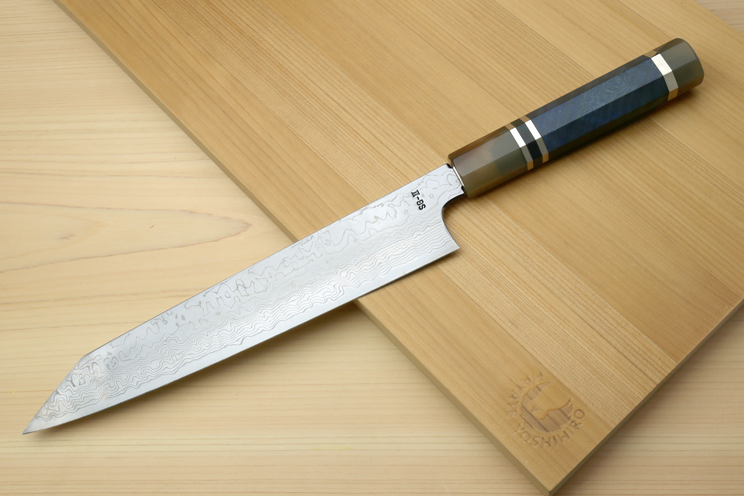 Utility-Kiritsuke chef knife laid across wood, blue handle and patterned damascus blade