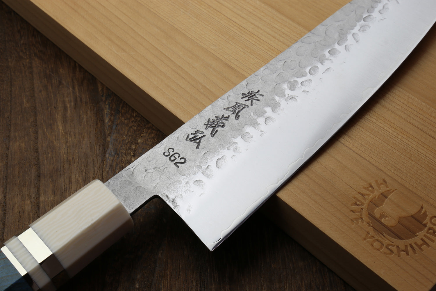 Hammered stainless gyuto knife blade close-up with etched markings and ocean blue handle