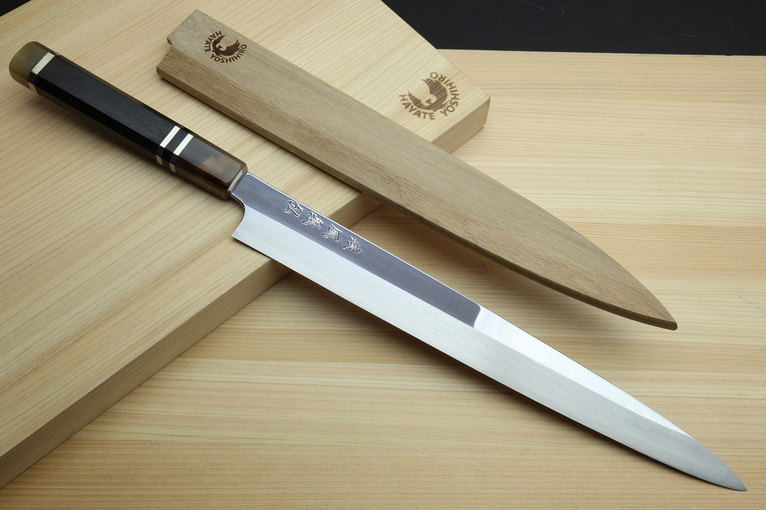 Yanagi sashimi knife on light wood with mirror blade and dark triple-ring ebony handle