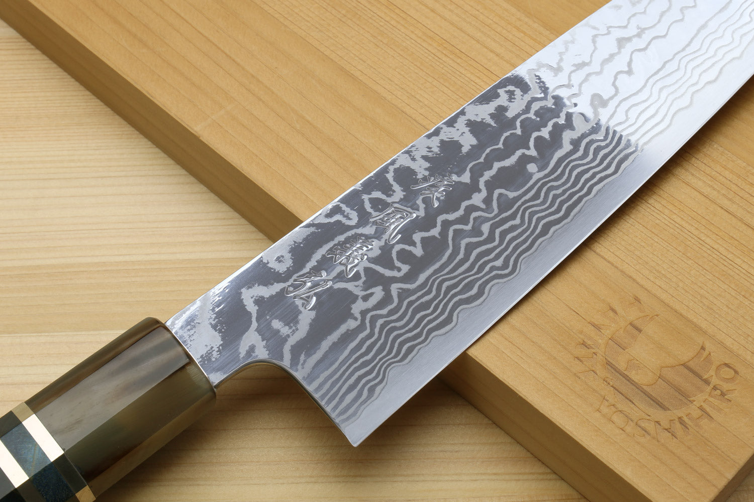 Gyuto chef knife close-up with wavy damascus blade and ocean blue handle bolster