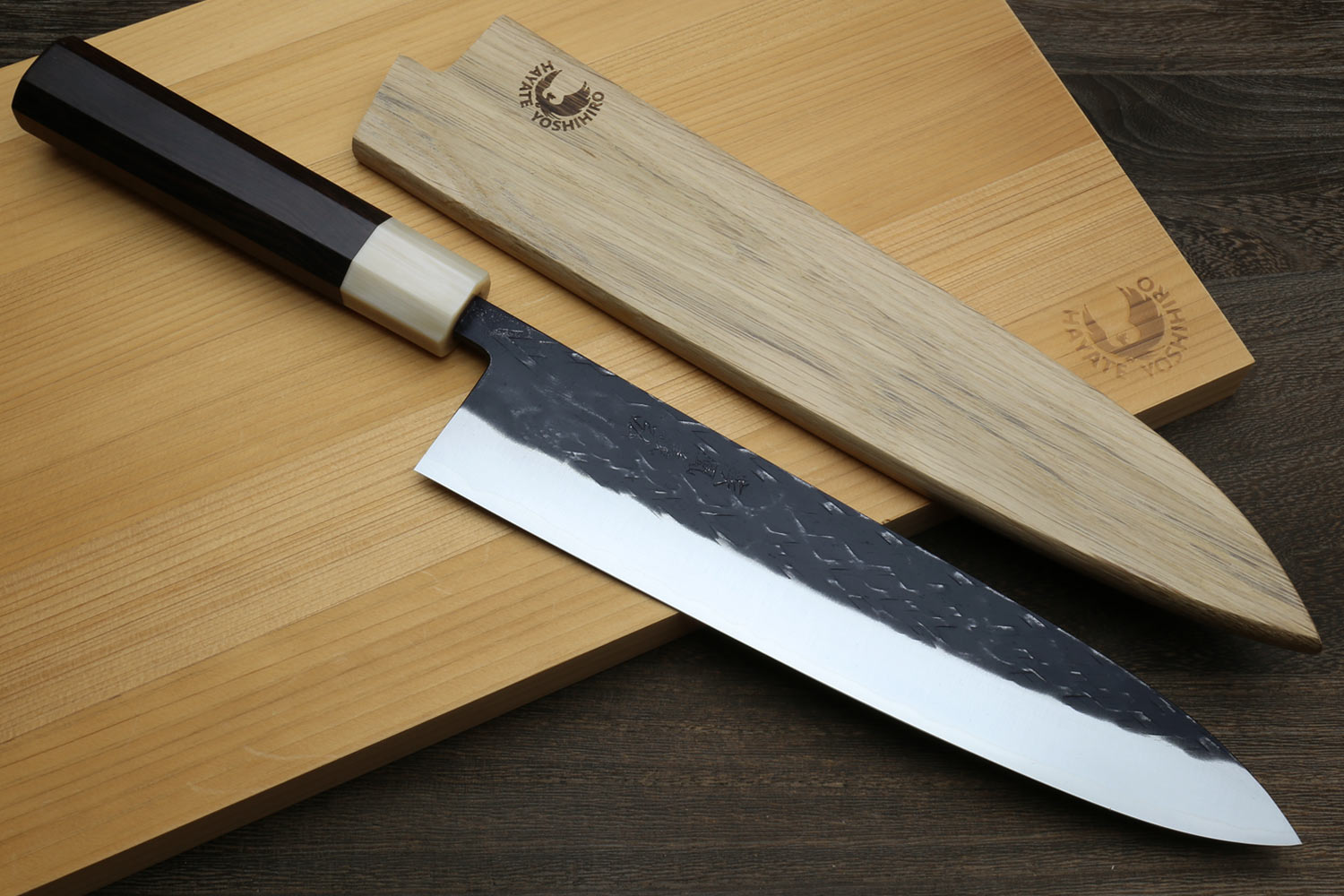 Gyuto chef's knife with dark handle, black-patterned blade and light wooden saya