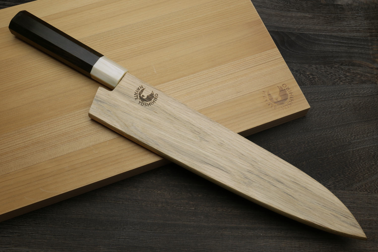 Gyuto chef's knife resting on wooden boards, dark handle and black-patterned blade