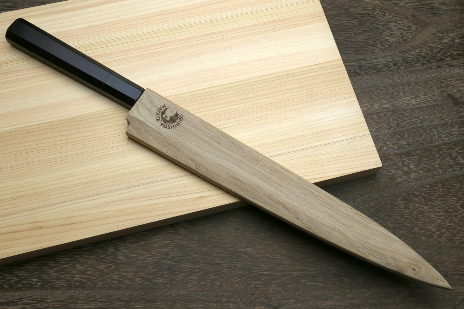 Yanagi sushi knife with black handle and steel damascus blade, beside wooden sheath
