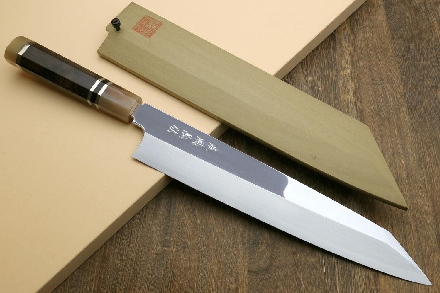 Kiritsuke Japanese knife with mirror blade, dark handle, and light wooden saya