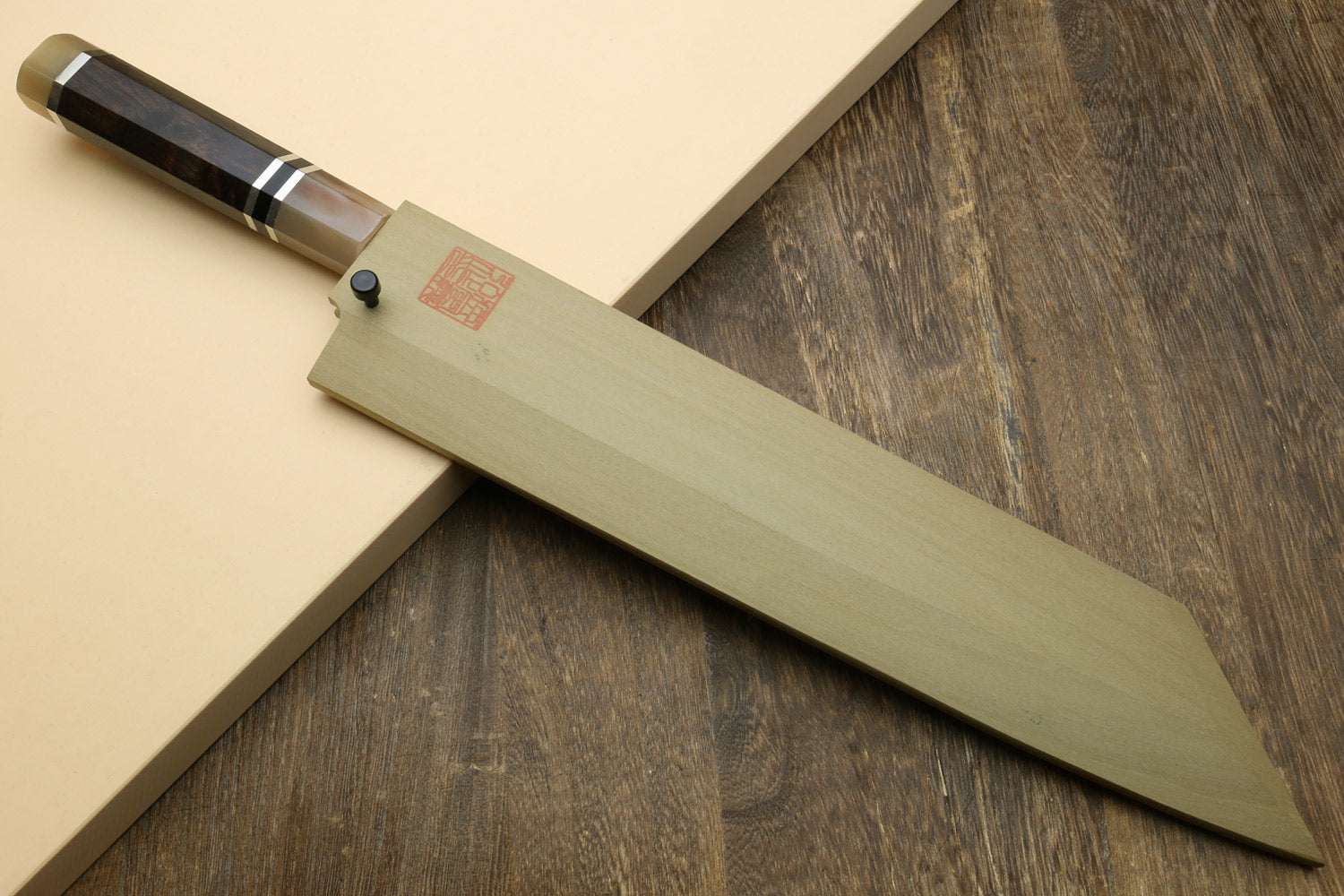 Kiritsuke Japanese knife on board with mirror blade and dark triple-ring handle