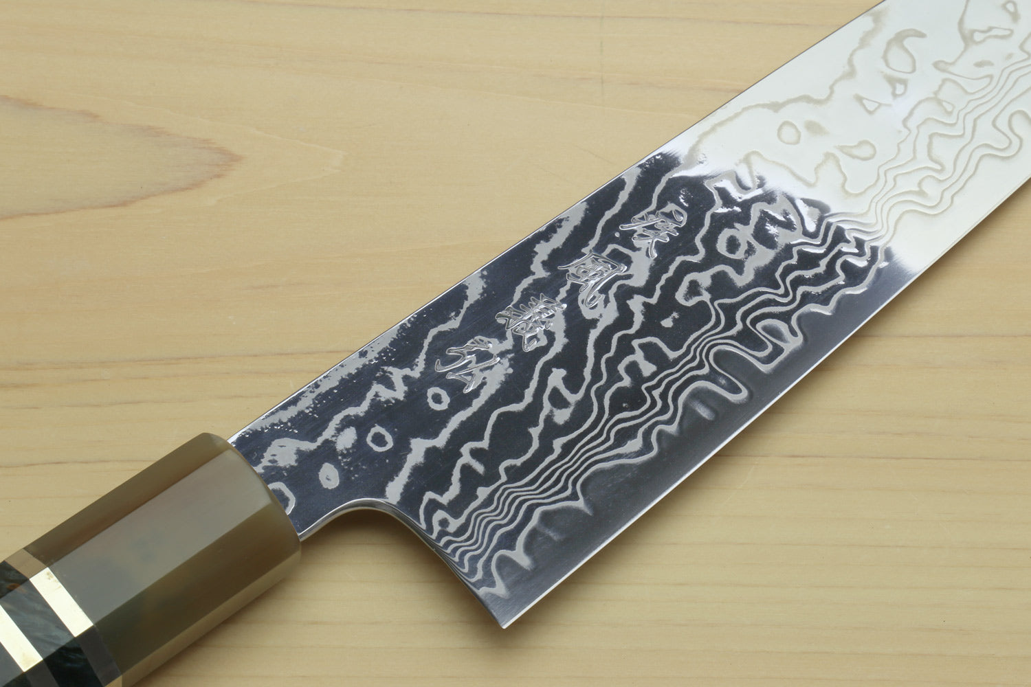 Chef gyuto knife close-up: dark Damascus blade with curved handle and scalloped edge