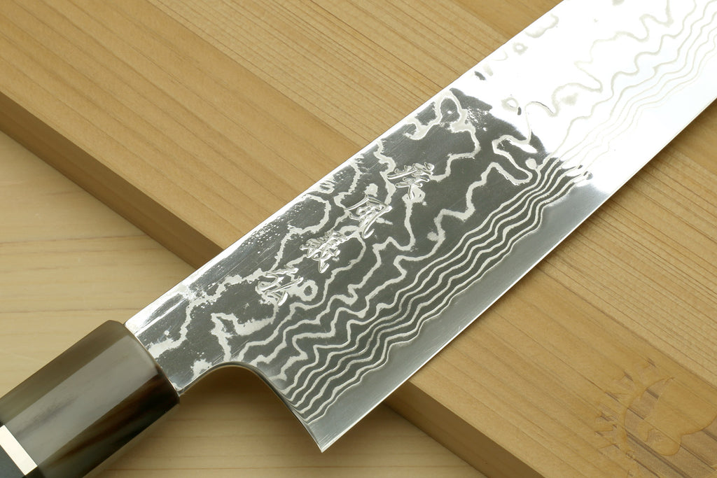 Damascus chef knife blade close-up with wavy pattern and part of blue octagonal handle