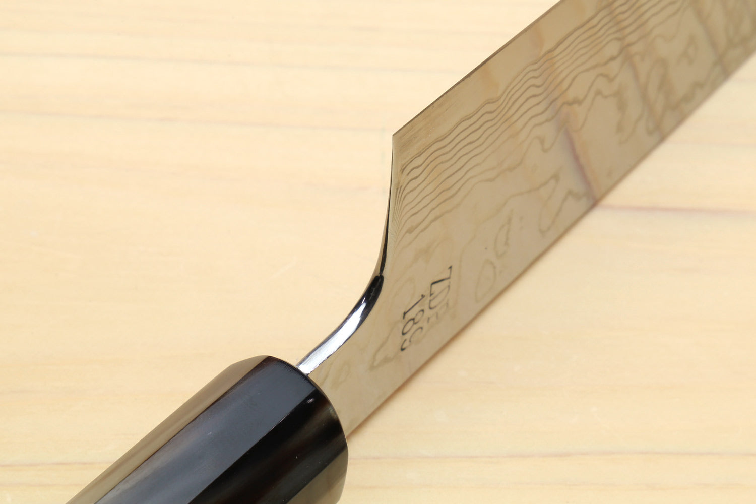 Damascus chef knife heel close-up with tang markings and dark guard