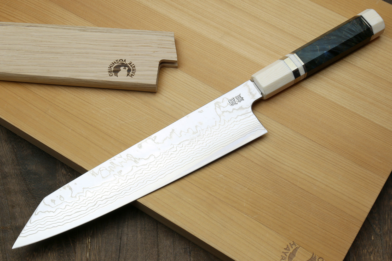 Kiritsuke chef knife with Damascus blade, ivory bolster, dark handle, beside wooden blocks