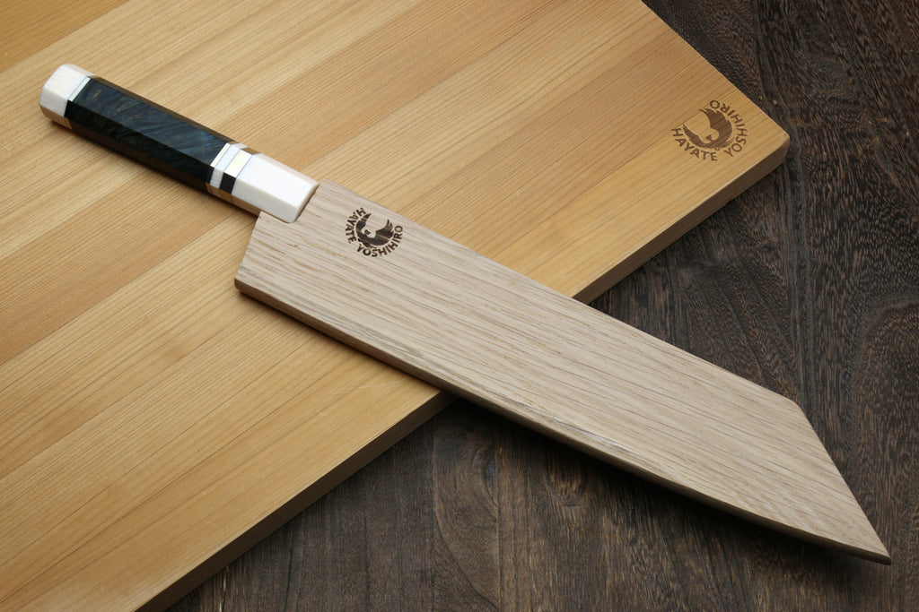 Kiritsuke chef knife with dark handle, ivory bolster, and Damascus blade on boards
