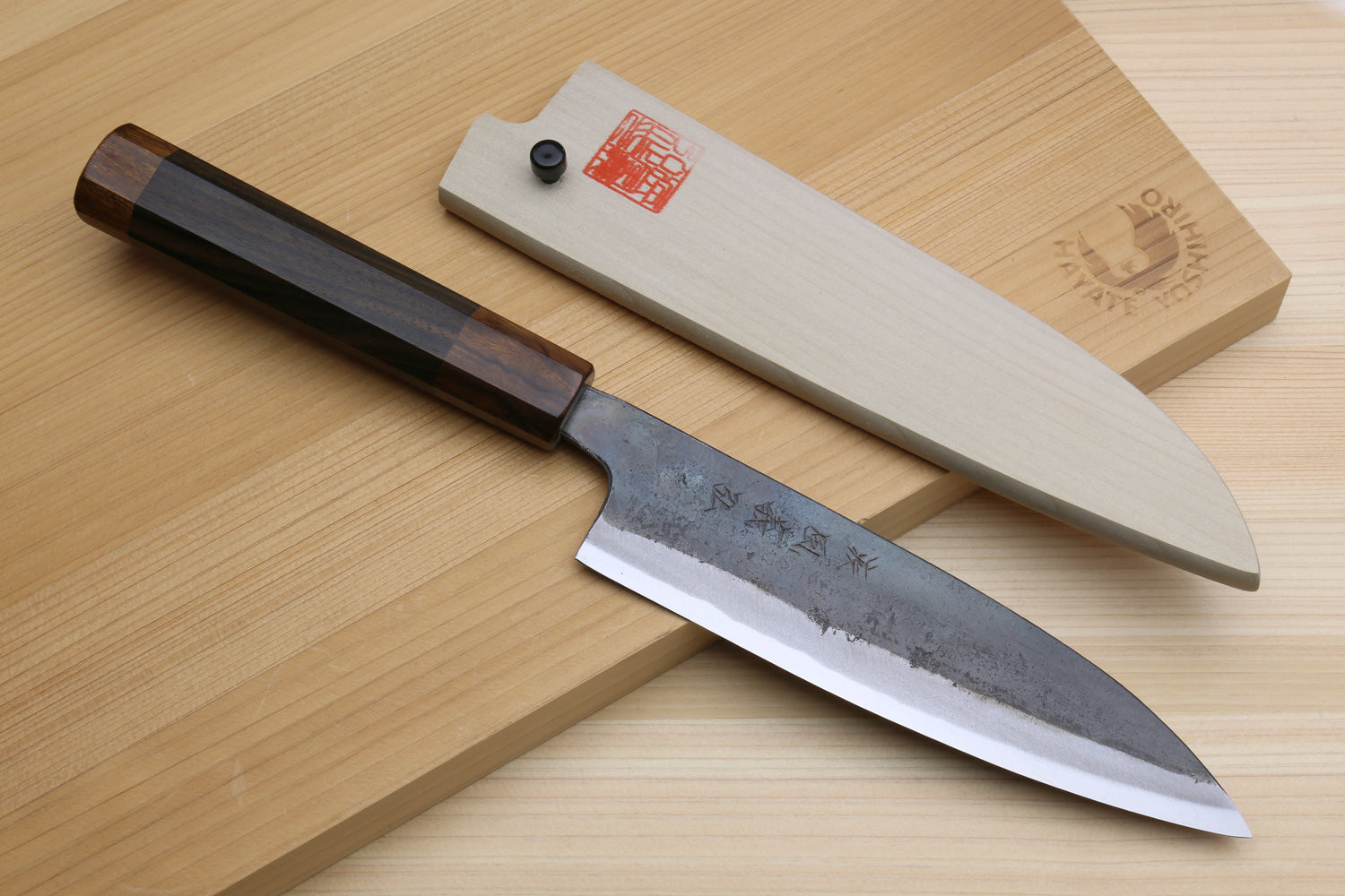 Petty utility knife with ebony handle and blue-gray kurouchi blade on wooden boards