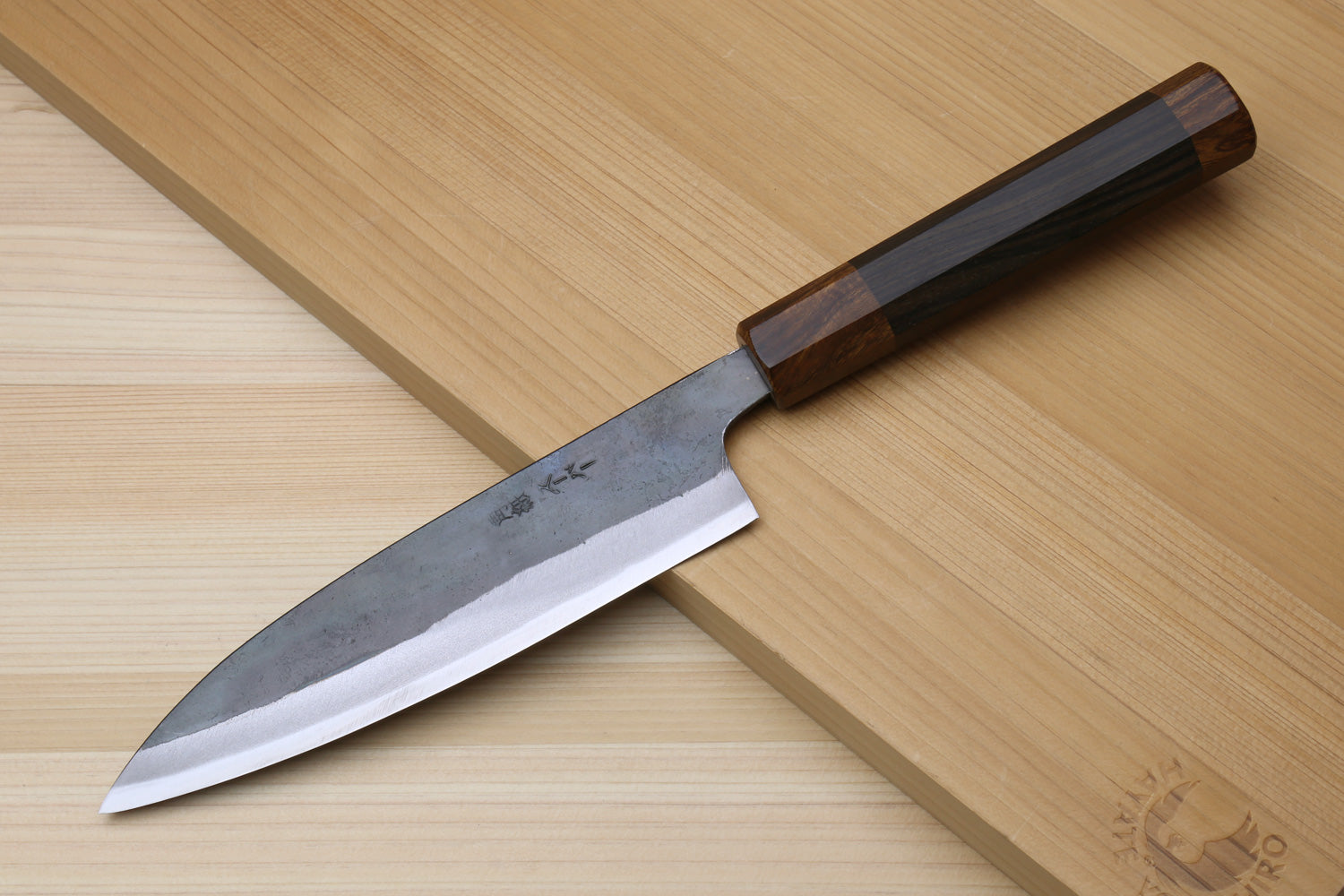 Petty utility knife with kurouchi-finished steel blade and ebony handle, angled view