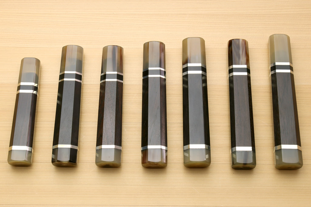 Chef knife handles lineup with horn bolster ends and black-and-white triple ring stripes