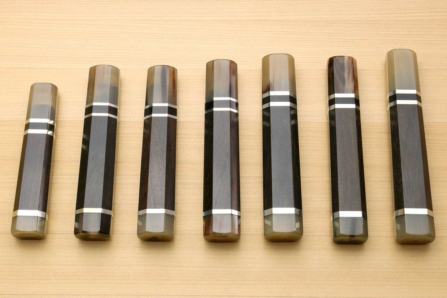 Chef knife handles lineup with horn bolster ends and black-and-white triple ring stripes