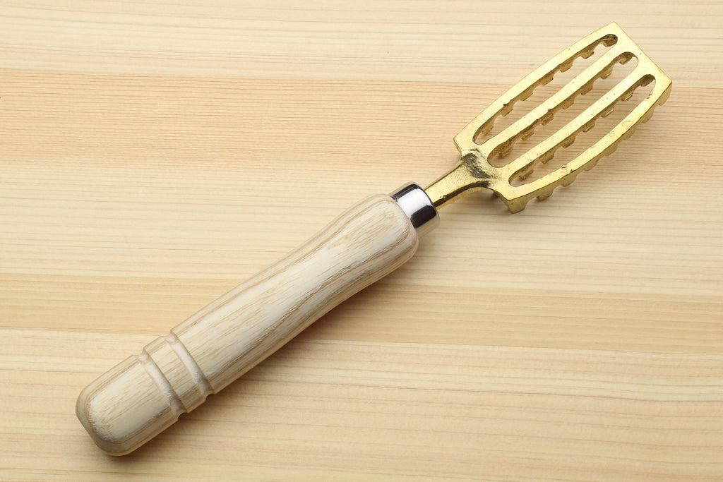 Large fish scaler tool with light wood handle and gold-toned slotted blade