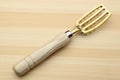 Large fish scaler tool with light wood handle and gold-toned slotted blade