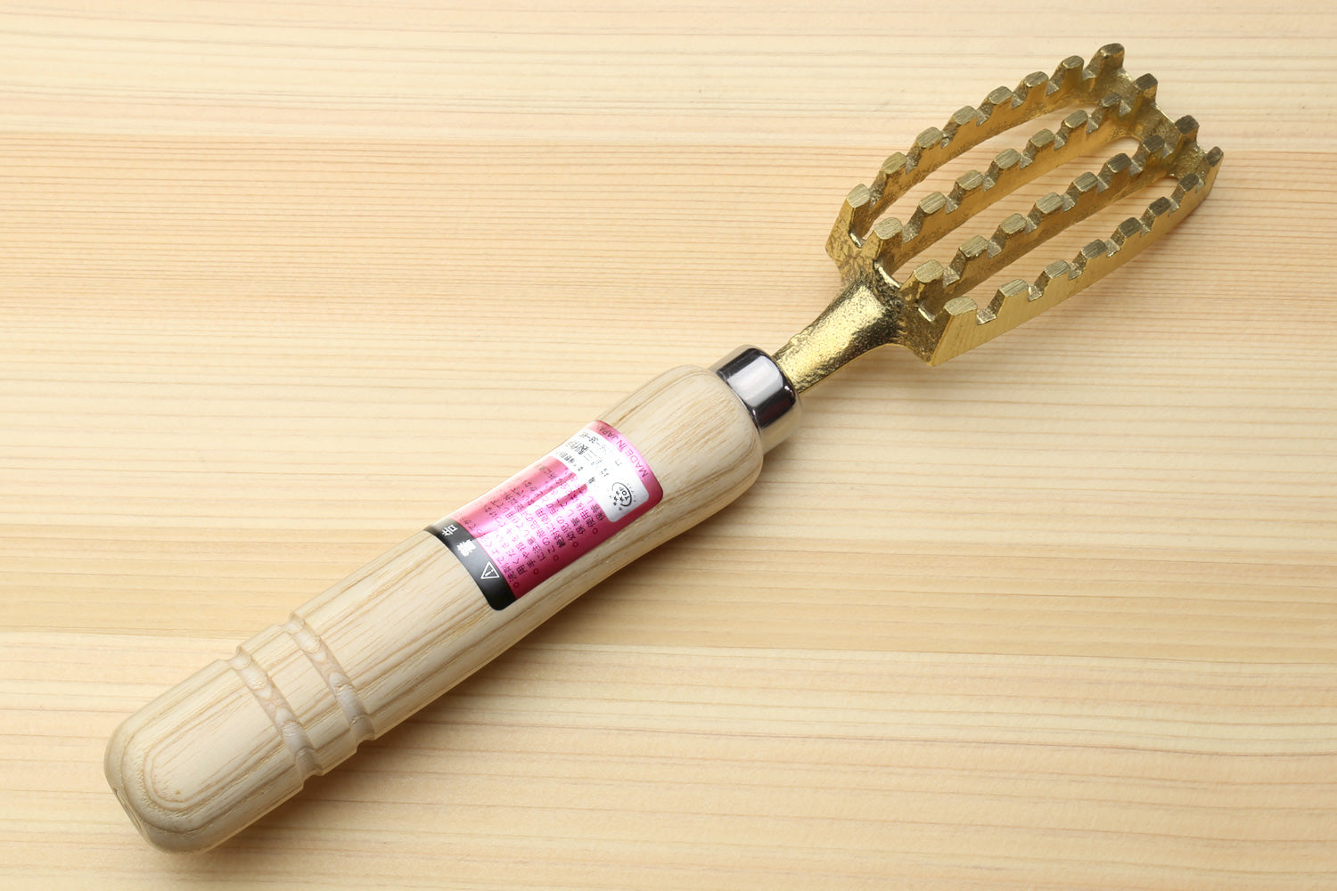 Large fish scaler tool with wood handle and gold-toned scaly head, pink label wrap