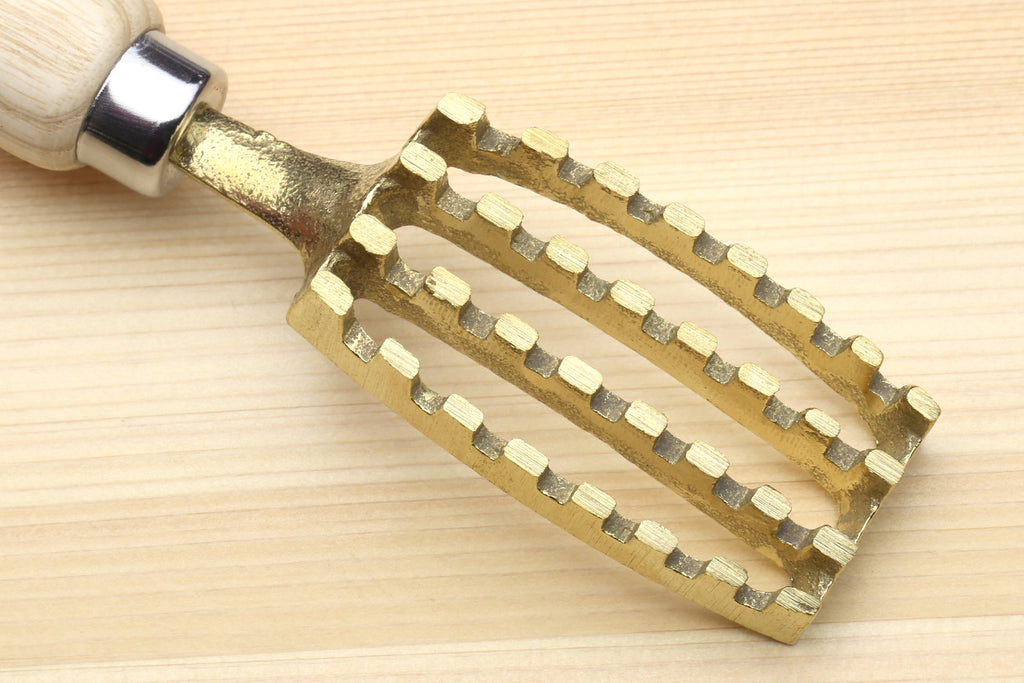 Large fish scaler tool head viewed from below, gold-toned scraping teeth on wood handle