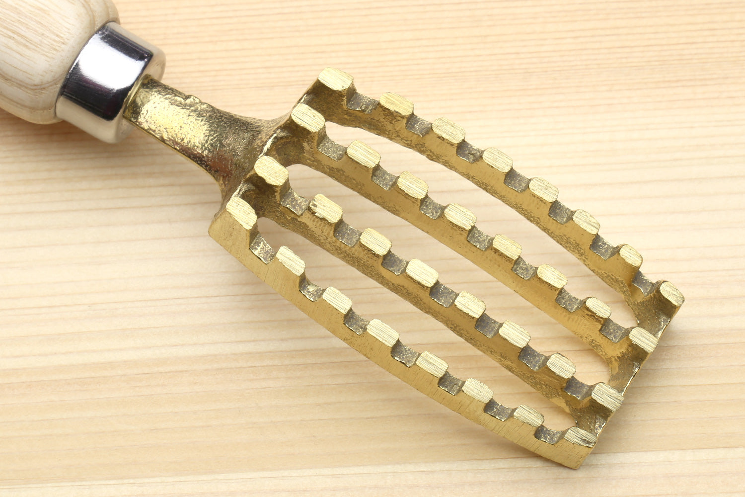 Large fish scaler tool head viewed from below, gold-toned scraping teeth on wood handle