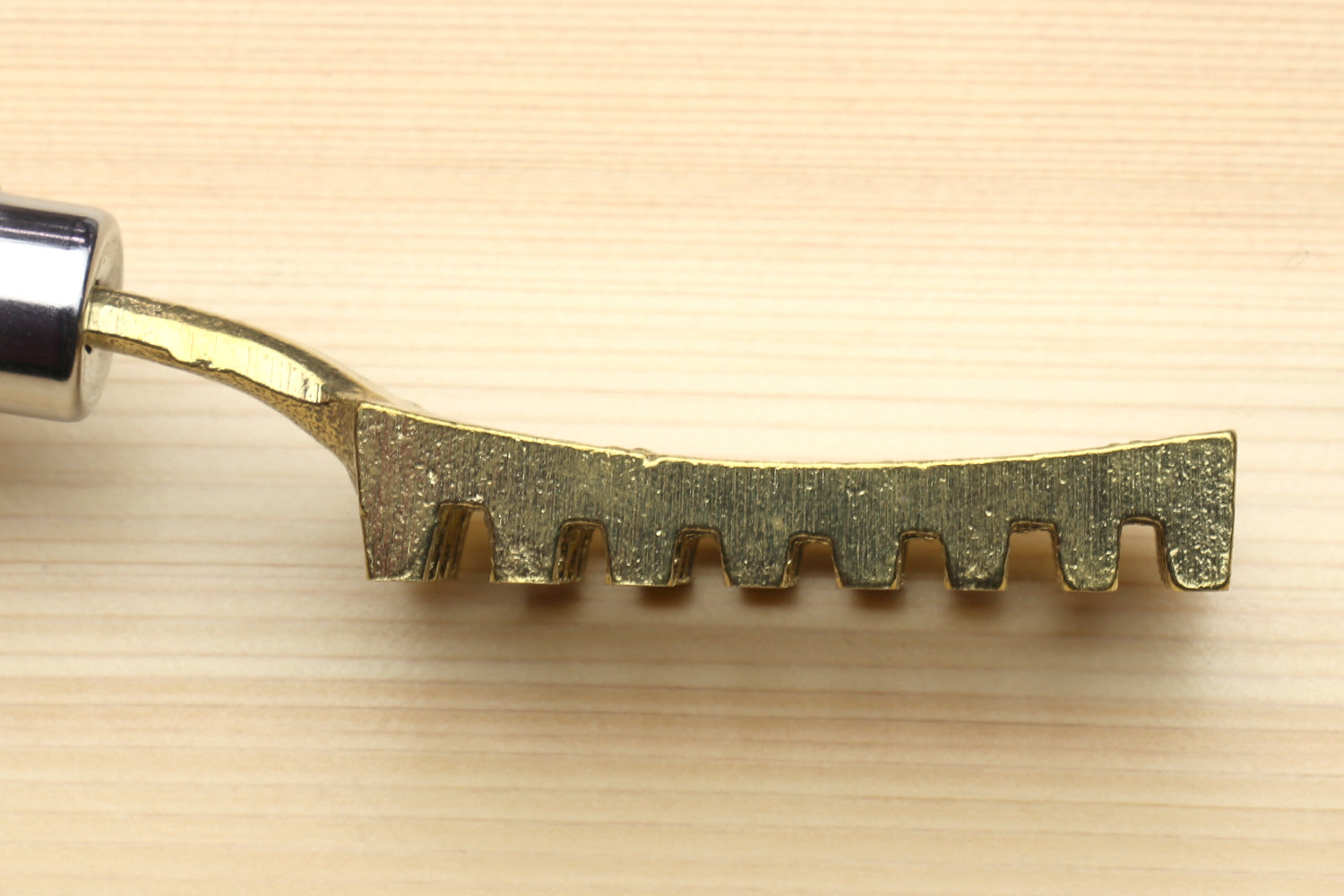 Large fish scaler tool blade end with serrated teeth and gold-toned finish