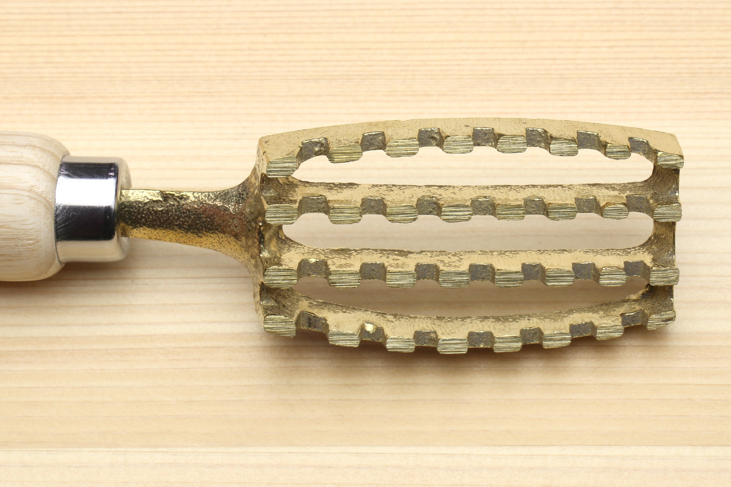 Large fish scaler tool close-up of ribbed gold-toned head attached to wood handle