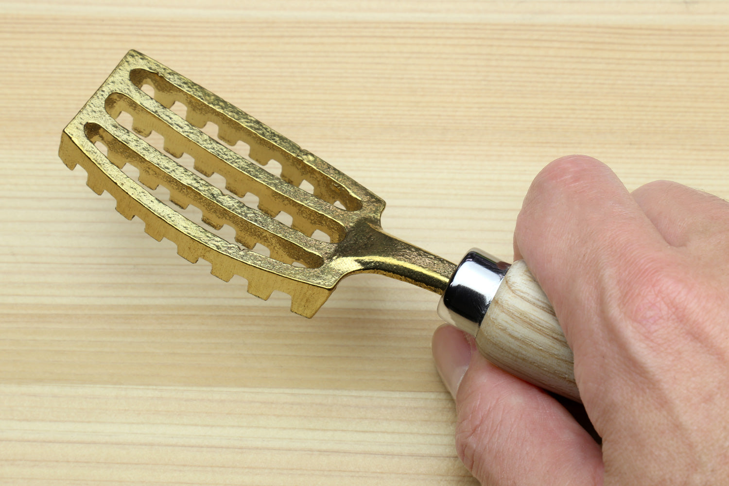 Large fish scaler tool in hand showing flat ribbed head and light wood handle