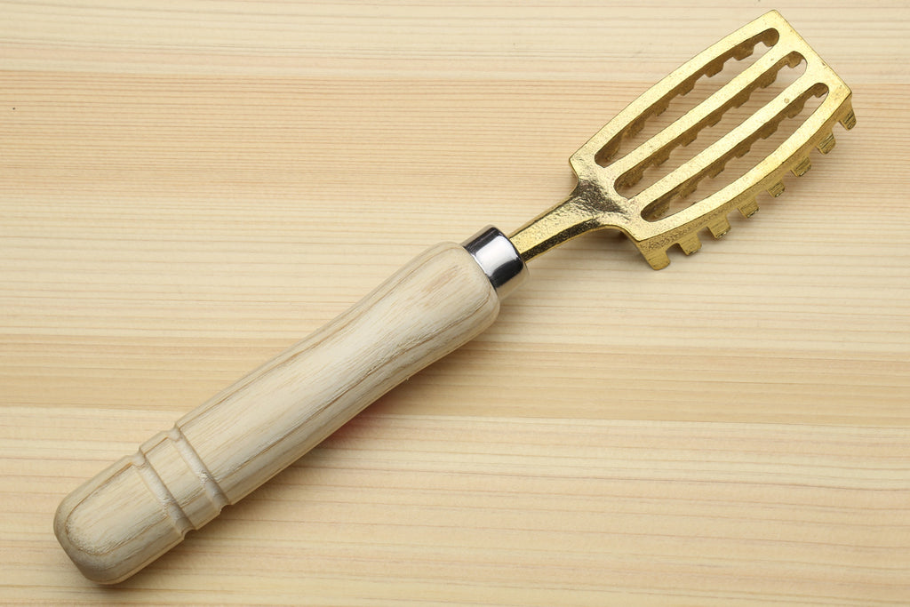 Fish scaler tool with light wood handle and gold metal head with raised ridges